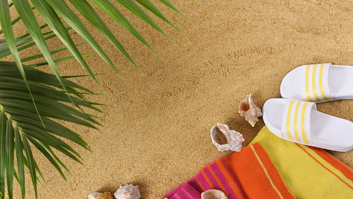 Beach background with palm leaves, towel and flip flops (studio shot - directional lighting and warm color cast are intentional).