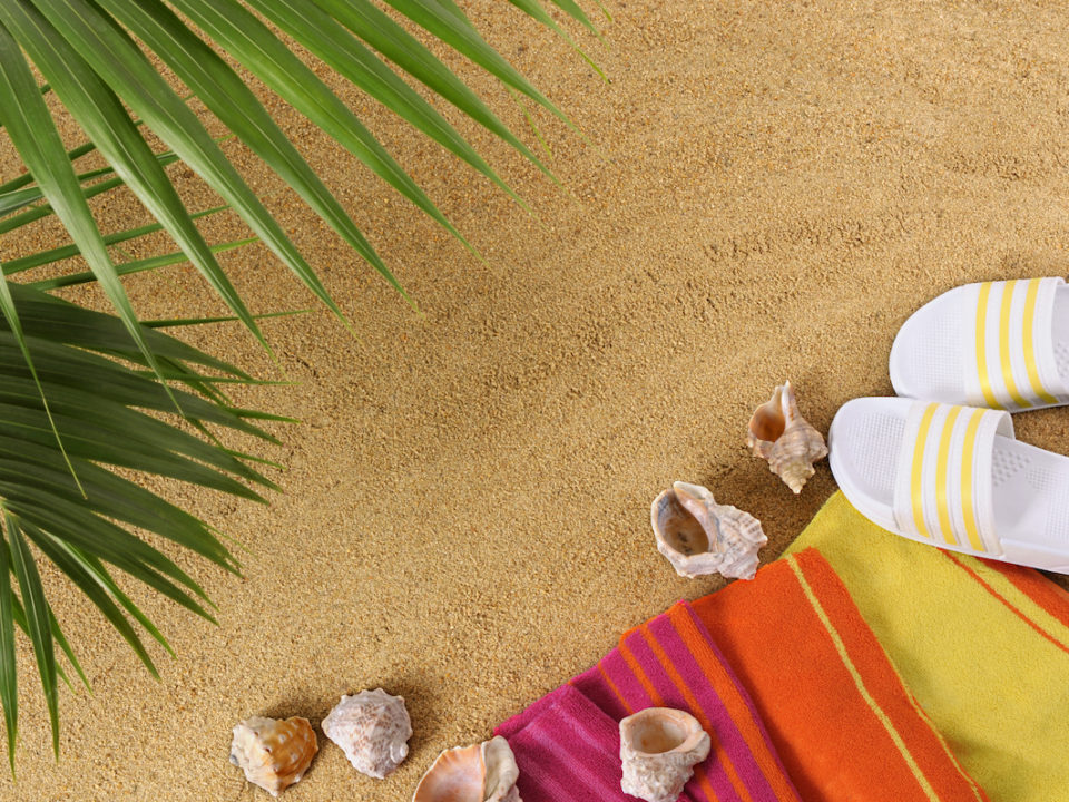 Beach background with palm leaves, towel and flip flops (studio shot - directional lighting and warm color cast are intentional).