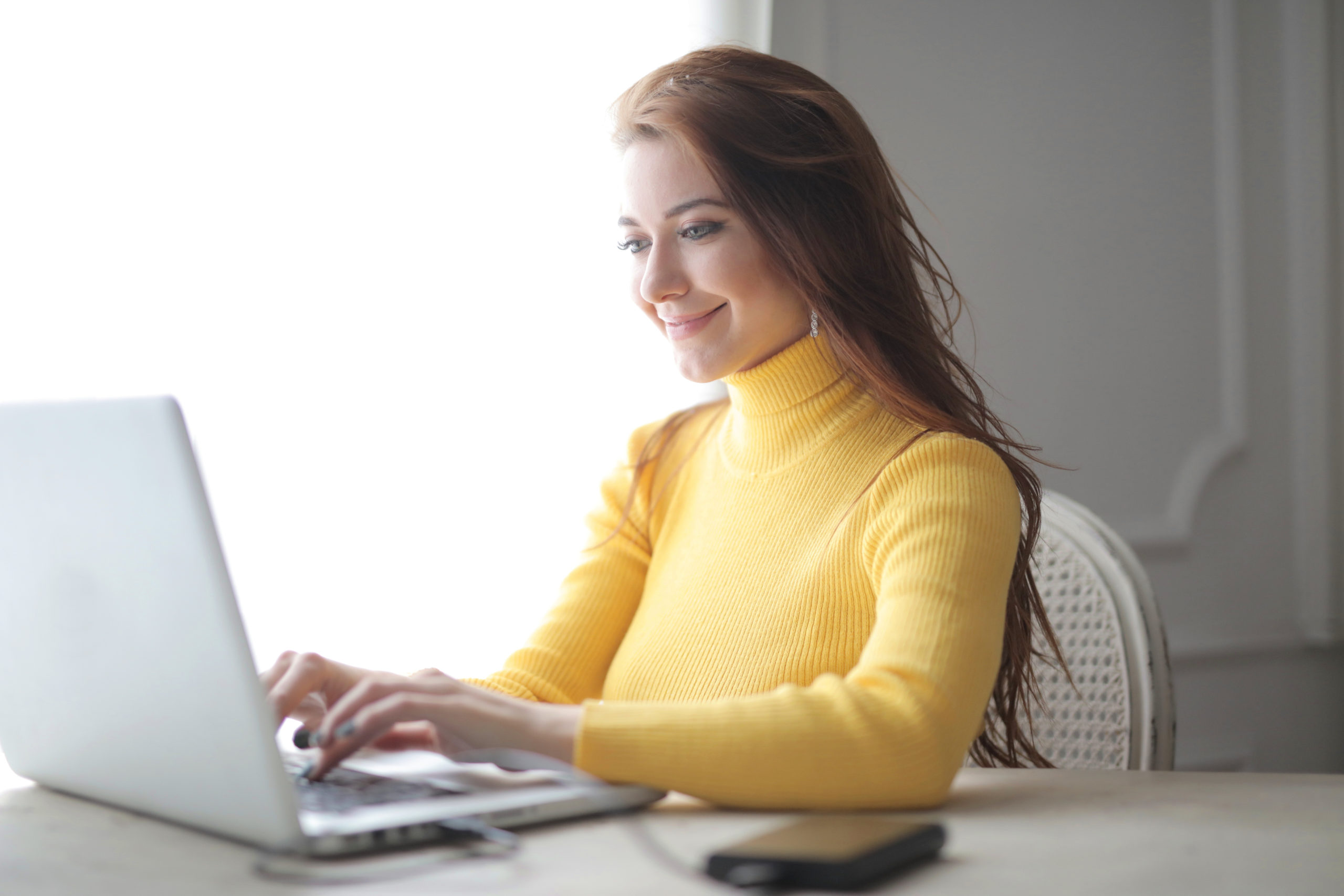 woman in yellow sweater typing on laptop