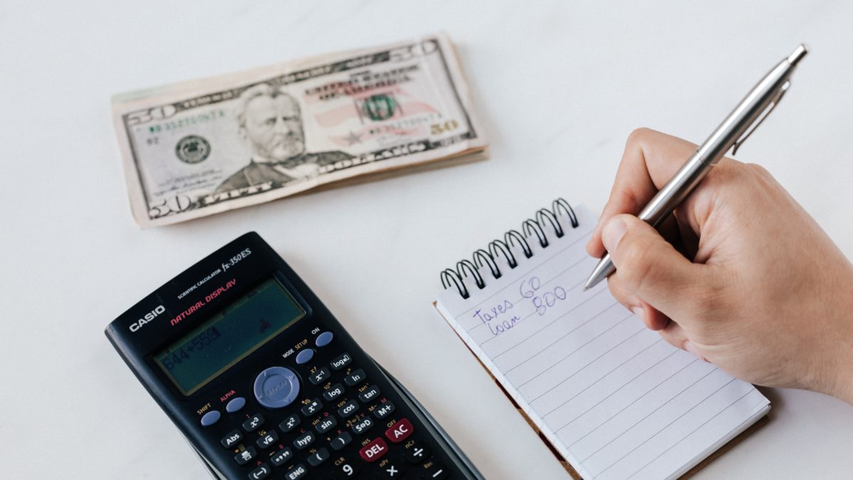 Person writing on notepad, calculator and money pictured.