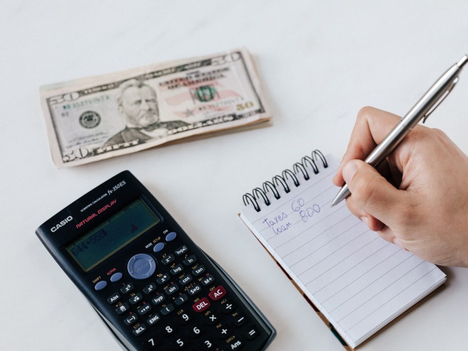 Person writing on notepad, calculator and money pictured.