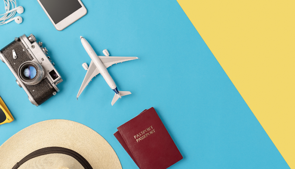 flatlay of plane, passport, beach hat, and sunglasses.