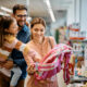 Little girl and her parents choosing backpack for school while shopping in store together.