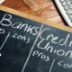 Banks vs. Credit Unions pros and cons written on a blackboard.