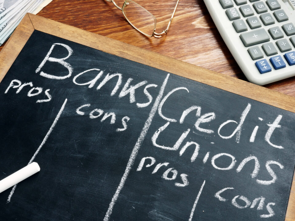 Banks vs. Credit Unions pros and cons written on a blackboard.