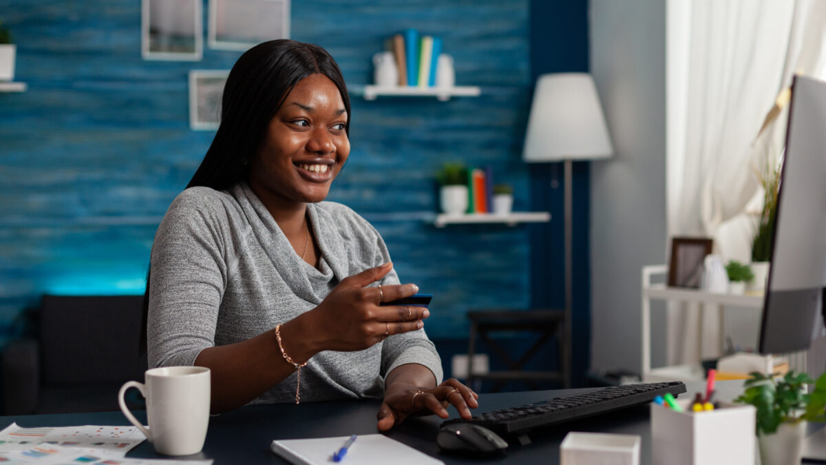 Person with credit card preparing to do shopping online on computer and smiling. Woman feeling excited about buying clothes on website, using banking money to make purchase on internet