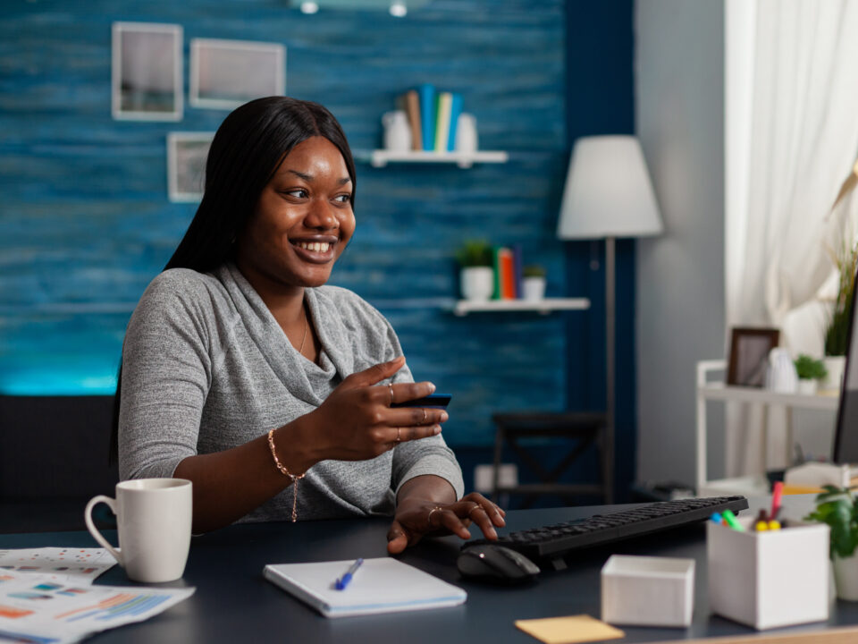 Person with credit card preparing to do shopping online on computer and smiling. Woman feeling excited about buying clothes on website, using banking money to make purchase on internet