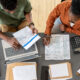 Overview of two young economists discussing financial papers and entering data while sitting by table at working meeting