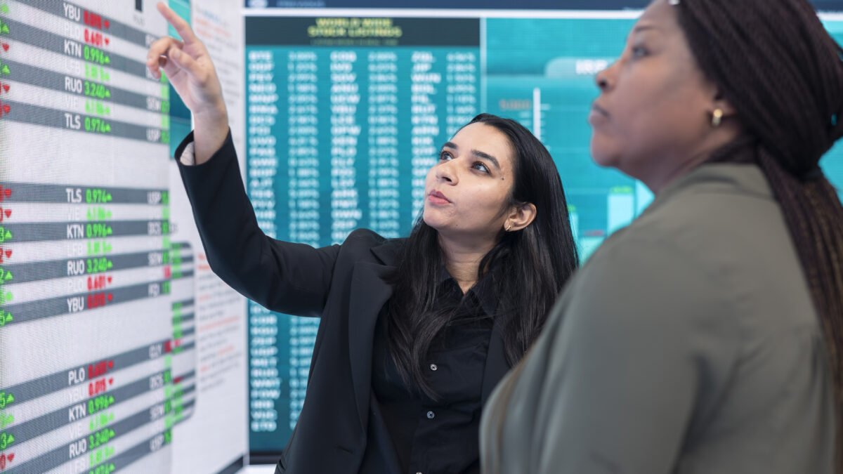 Diverse team of employees examine infographics on a big screen to evaluate supply and demand, ways of increasing organizational budget and develop the business internationally.