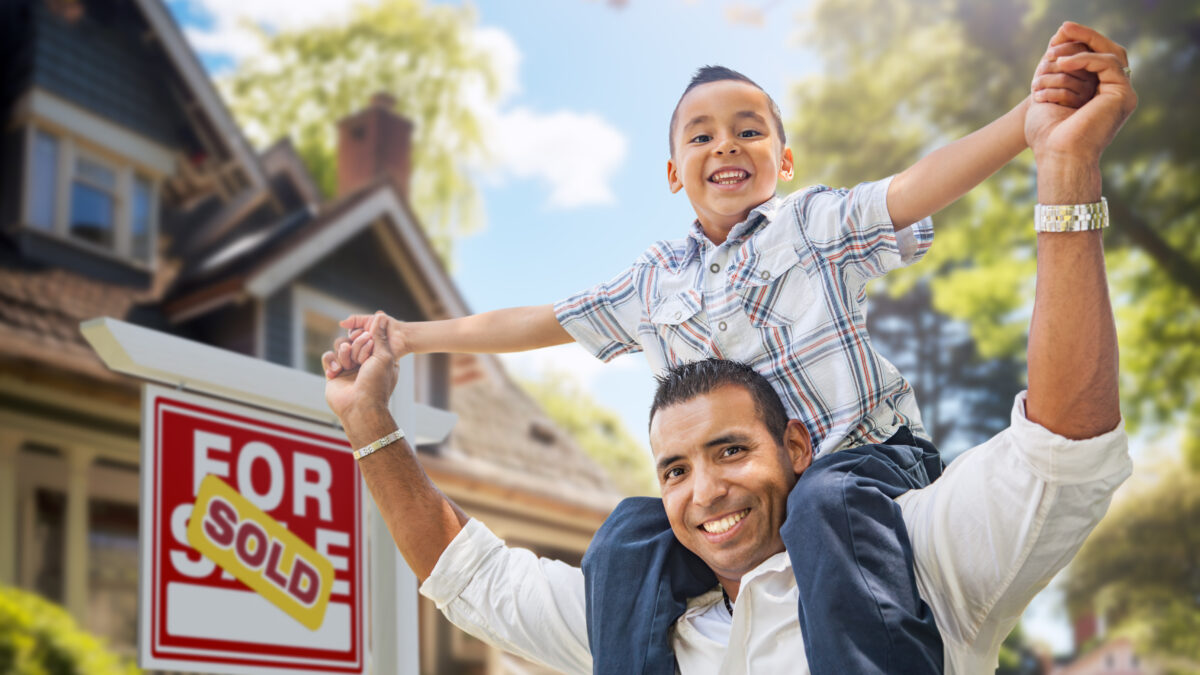 Happy Father and Son Riding Piggyback In Front of New House and Sold For Sale Real Estate Sign.
