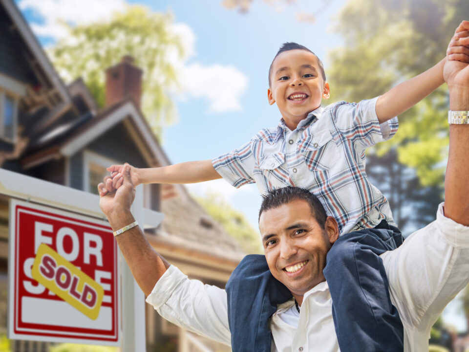 Happy Father and Son Riding Piggyback In Front of New House and Sold For Sale Real Estate Sign.