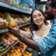 happy asian woman looking at african american man near fruits in store