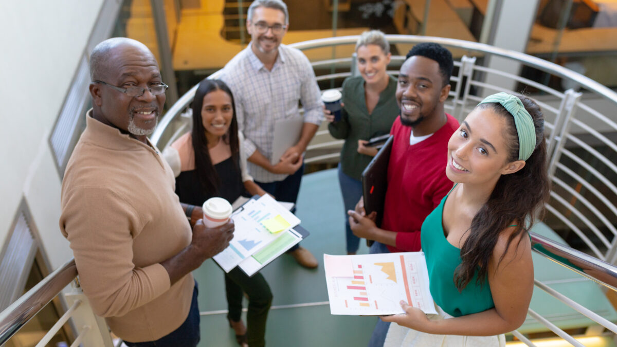 High angle portrait of smiling multiracial male and female advisors standing at staircase in office. unaltered, business, teamwork and modern office concept.