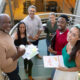High angle portrait of smiling multiracial male and female advisors standing at staircase in office. unaltered, business, teamwork and modern office concept.