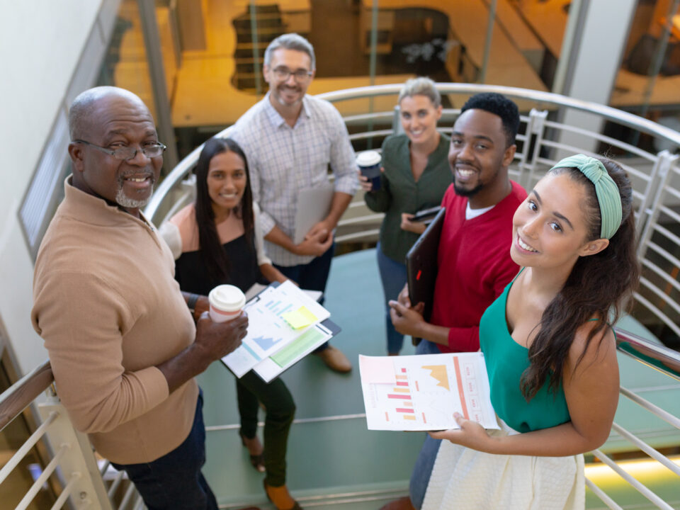 High angle portrait of smiling multiracial male and female advisors standing at staircase in office. unaltered, business, teamwork and modern office concept.